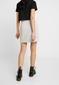 Grijs textured minirok met een licht uitlopende zoom, gecombineerd met een cropped zwart t-shirt en zwarte veterboots tot de enkel.