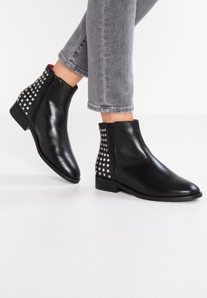 Svart läderankelboots med en snygg design, spetsig tå och nitar på klacken. Avslutade med en låg, platt sula.