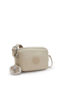 Beige crossbody bag made of textured fabric, featuring a geometric pattern, a round logo patch, and a plush monkey charm. Adjustable strap included.