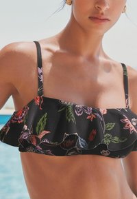 Crni bikini top s naboranim rubom, s vibrantnim cvjetnim uzorkom u nijansama ružičaste, crvene i zelene. Tanji podesivi remen.