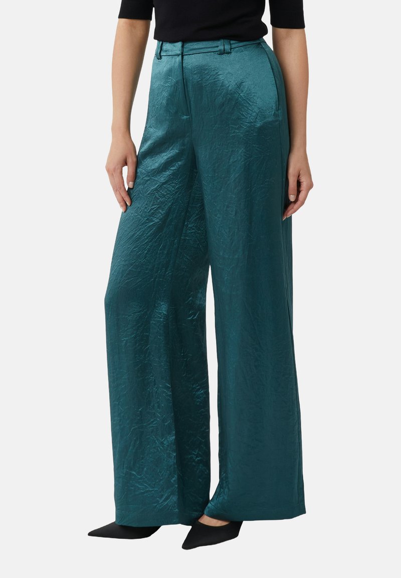 Teal, wijde broek gemaakt van een glanzende, gestructureerde stof, met een hoge taille en riemlussen, gecombineerd met zwarte schoenen.