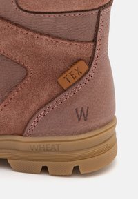 Brun mocka stövel detalj med strukturerad yta, rosa sömmar, en läderetikett med "TEX" och "WHEAT" präglat på sålen.