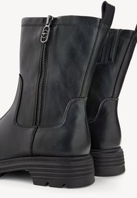 Botas de tobillo de cuero negro con cremallera lateral, que cuentan con una superficie texturizada, tacón reforzado y una suela de goma resistente para mayor tracción.