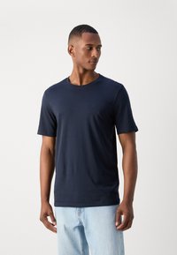 Marinblå, kortärmad t-shirt av mjuk bomull, med rund halsringning och en liten logotyp på bröstet, ihop med ljusa jeans.