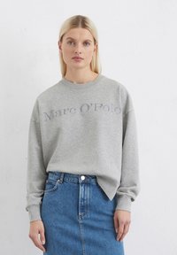 Felpa grigia con collo a girocollo a costine e spalle scese, con logo "Marc O'Polo" in grigio chiaro. Abbinata a una gonna di jeans.