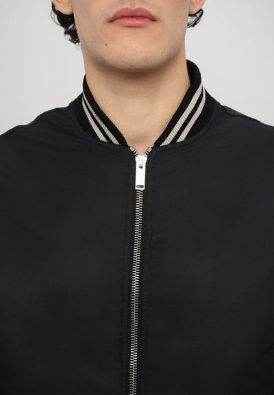 Giubbotto bomber nero con chiusura a zip, colletto a costine con strisce bianche e nere, e una texture di tessuto liscia e opaca.