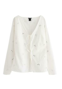 Vit långärmad blus med V-hals, som har blommönster broderi och detaljer med pärlor. Lättviktig tyg med knytning fram.