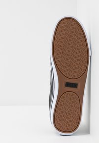 Svart sneaker med vita ränder; gummisula med fiskbensmönster och en tan-färgad botten; präglad "POLO"-logga på sulan.