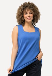 Top senza maniche blu con scollatura quadrata, realizzato in tessuto morbido, caratterizzato da un taglio morbido e orlo dritto, indossato con pantaloni scuri.