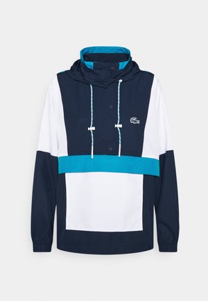 Veste à capuche bleu marine, blanche et turquoise avec boutons à l'avant, capuche à cordon de serrage, poignets élastiques et un petit logo crocodile brodé sur la poitrine.