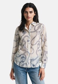 Leichte, cremefarbene Bluse mit einem blauen Seil- und Motivmuster, mit Knöpfen an der Vorderseite und langen Ärmeln, präsentiert vor einem weißen Hintergrund.