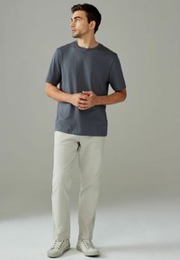 Mørkegrå kortærmet t-shirt kombineret med lysebeige bukser og hvide sneakers, sat mod en neutral baggrund.