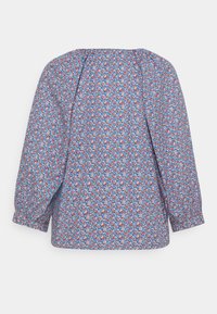 Blouse florale bleue avec manches longues bouffantes. Présente un motif de fleurs rouges et blanches, avec une coupe ample et un col large.