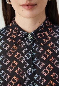 Crna košulja s gumbima, koja sadrži gradijentni uzorak isprepletenih oblika u pastelnim bojama. Glatka tekstura, klasična kragna, vidljivi gumbi.