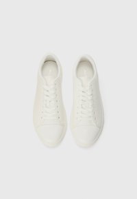 Hvite sneakers med en glatt læroverdel, rund tå, flate snører og minimal sømdetaljering. Mykt stofffôr på innsiden.