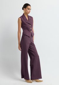 Violet sleeveless vest with a notched collar and gold buttons, paired with wide-leg pants. Both pieces feature a textured fabric.
