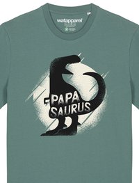 T-shirt en coton turquoise avec une silhouette de dinosaure noire et le texte "PAPA SAURUS" sur un fond graphique circulaire crème.