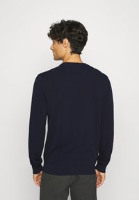 Navy blue sweater, long sleeves, crew neck, ribbed cuffs and hem, smooth texture, fitted design, viewed from the back.