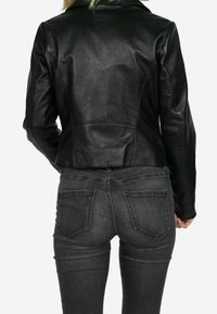 Zwarte leren jas met een aansluitend ontwerp, gladde textuur en zichtbare stiknaden. Gecombineerd met donkergrijze spijkerbroek met achterzakken.