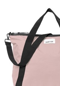 Rosa Tragetasche mit schwarzen Trägern, ausgestattet mit einem Reißverschluss und einem "DAY ET"-Etikett an der Seite. Einfaches und funktionales Design.
