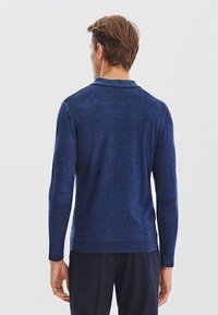 Granatowy sweter dzianinowy z długimi rękawami i kołnierzem, z gładką teksturą i ściągaczem u dołu. Widok z tyłu.