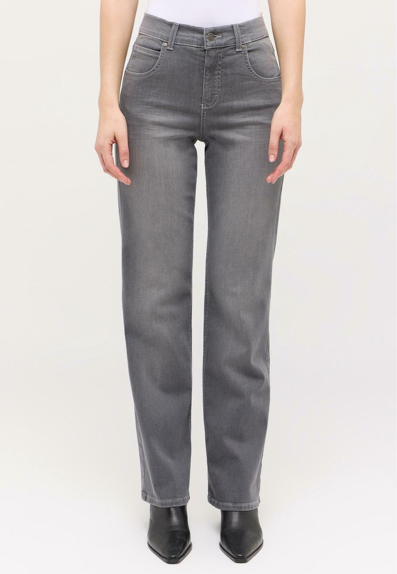 Femme portant un jean gris droit taille mi-haute et des bottines noires à bout pointu, debout les mains détendues le long du corps.
