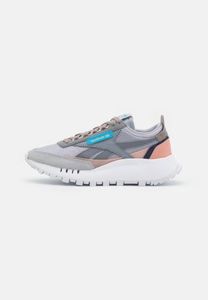 Baskets Reebok grises et roses avec semelle épaisse blanche, textures en maille et daim, lacets beiges et étiquette de logo bleue sur le côté.