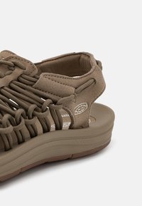 Brown multi-strapped sandal with elastic design, soft suede upper, cushioned footbed, and textured rubber sole for grip.