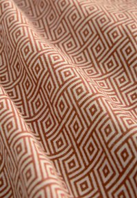 Tessuto decorato con un motivo geometrico di quadrati incastrati nei colori ruggine e crema, con una texture liscia e una leggera lucentezza.