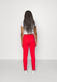 Röda sportbyxor med en smal passform och elastisk midja, med vita sidostreck. Bärs tillsammans med en figurnära vit topp.