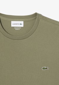T-shirt verde oliva realizzato in 100% cotone Pima, con colletto a girocollo, maniche corte e un piccolo logo ricamato a forma di coccodrillo.