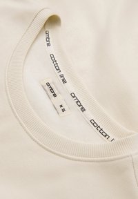 Chemise en coton beige à col ras du cou, présentant un col côtelé et une étiquette de marque "ombre cotton line" avec la taille M (UE 48).