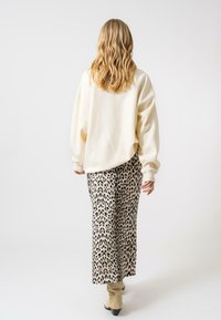 Sweatshirt surdimensionné crème associé à un pantalon large imprimé léopard, avec des taches noires et une texture douce. Des chaussures beiges unies complètent le look.