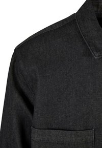 Giubbotto in denim nero con collare classico, una tasca sul petto e una finitura in tessuto testurizzato.