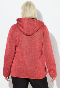 Haut à capuche en polaire rouge avec une apparence texturée, doté d'une capuche et d'une bordure contrastante orange le long de l'ourlet et des poignets.
