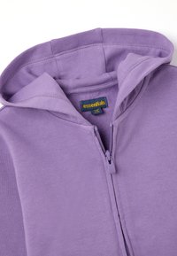 Felpa con zip di colore viola realizzata in tessuto morbido, dotata di cappuccio, polsini elasticizzati e un'etichetta con la scritta "essentials". Texture liscia e design semplice.