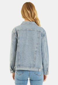 Giubbotto di jeans di colore azzurro chiaro, con un motivo a pois, colletto classico e dettagli con bottoni. La vista posteriore mostra una vestibilità rilassata.