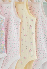 Dziecięce podkoszulki na ramiączkach z małymi kwiatowymi wzorami w pastelowych kolorach wiszące na drewnianych wieszakach.