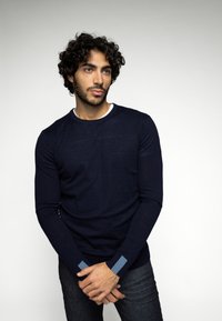 Pulover lung cu mânecă din lână de culoare bleumarin, fabricat dintr-un tricot moale, având un guler alb tip crew și accente albastre la manșete. Purtați-l cu blugi din denim închisi la culoare.