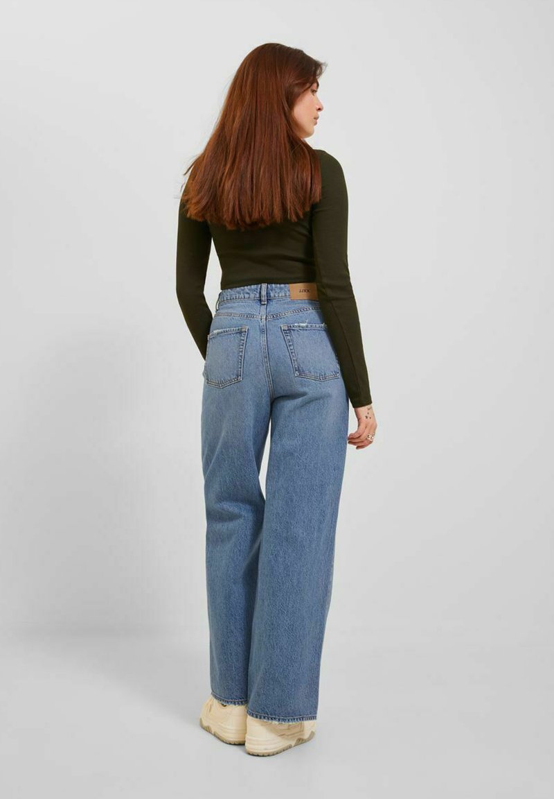 Jeans a vita alta e gamba larga in denim blu chiaro, con tasche posteriori e una patch in pelle del marchio, abbinati a un top fitted nero a maniche lunghe.