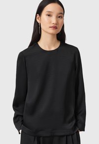 Svart långärmad blus i mjukt material med rundad halsringning. Har en avslappnad passform och subtil textur, lämplig för olika tillfällen.