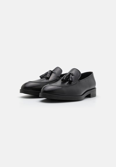 Les mocassins en cuir noir disposent d'une finition lisse, de détails en couture, d'un design à enfiler et de pampilles décoratives sur le devant. Talon bas empilé.