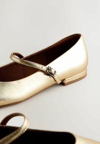 Goldfarbene, metallische Ballettschuhe mit runder Zehenpartie, ausgestattet mit einem Riemen und Silber-Schließe, flachem Absatz und glatter Oberfläche.