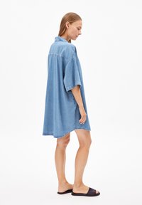 Lichtblauw denim shirtjurk met korte mouwen, een kraag en een relaxte pasvorm. Kenmerkt zich door een gebogen zoom en wordt gedragen met zwarte slippers.