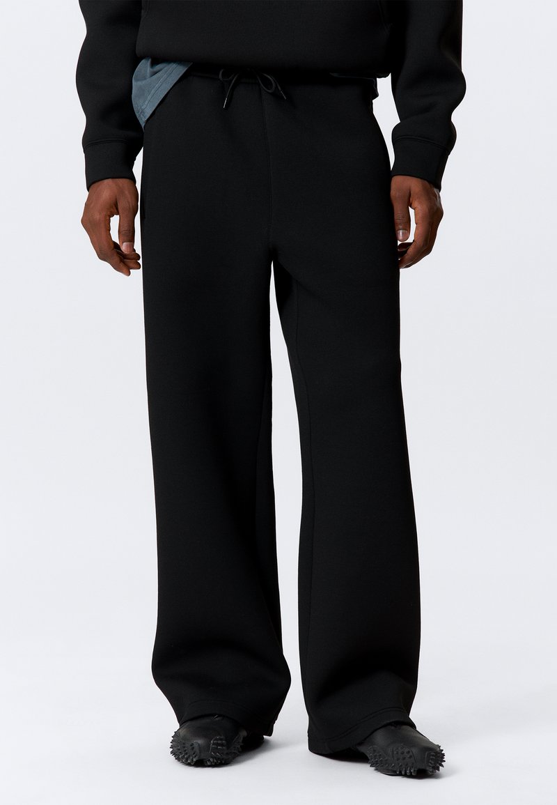 Black wide-leg sweatpants with a soft texture, featuring a drawstring waist and side pockets, paired with textured black footwear.