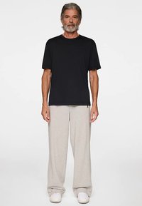 Musta pyöreäkauluksinen t-paita yhdistettynä vaaleanharmaisiin, leveälahkeisiin housuihin. Asussa on rento istuvuus ja pehmeä kangas. Valkoiset kengät viimeistelevät kokonaisuuden.