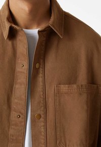 Brązowa kurtka z bawełny z domieszką, z kołnierzykiem, z zapięciem na guziki i przednią kieszenią. Teksturowana tkanina o subtelnym wzorze w jodełkę.