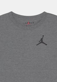 T-shirt in cotone grigio con colletto rotondo, caratterizzato da un logo Jumpman ricamato in nero sul petto e il testo "JORDAN" sopra in rosso.