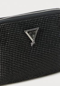 Pochette nera con zip coperta di piccole perline lucide e con un logo triangolare argento di Guess Girl sulla parte frontale.