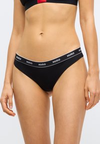Μαύρο βαμβακερό στρινγκ εσώρουχο με ελαστική ζώνη μέσης με λογότυπο σε λευκό χρώμα. Στενή γραμμή με ελάχιστη κάλυψη.